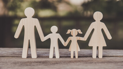 A photograph of wooden family figurines arranged in a line on a weathered wooden surface.