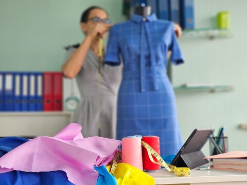 Designer works on a blue dress with a dress form in a sewing studio filled with colorful fabrics - Powered by Adobe