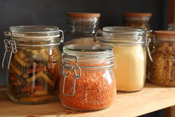 Glass jars with different products on wooden shelf, closeup