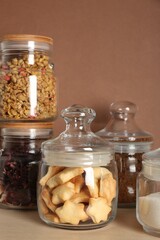 Glass jars with different products on wooden table against brown background, closeup