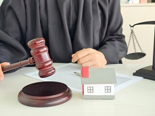 Legal proceedings with judge gavel, model house, and balance scale on the table in a courtroom