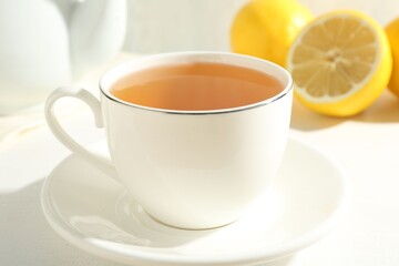 Aromatic tea in cup and lemons on white table, closeup