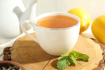 Aromatic tea in cup, lemons, mint and teapot on table, closeup