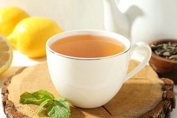 Aromatic tea in cup, lemons, mint, dry leaves and teapot on table, closeup