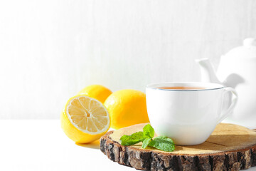Aromatic tea in cup, lemons, mint and teapot on white table, closeup. Space for text