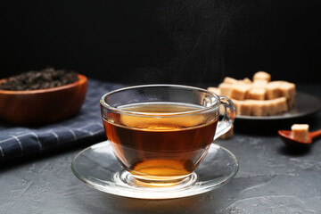 Aromatic tea in glass cup, brown sugar and dried leaves on black table, closeup