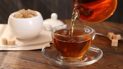 Pouring aromatic black tea into glass cup at wooden table, closeup