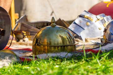 Golden Roman legionary helmet lying on wool blanket beside armor parts during outdoor historical reenactment on a sunny day.