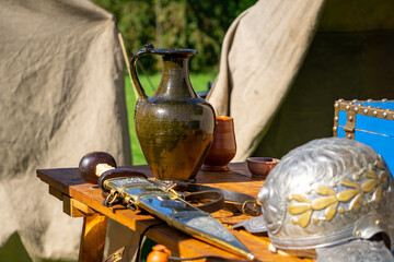 Silver Roman legionary helmet, gladius in decorated sheath and ceramic jug on wooden table in...