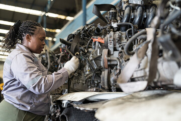 Automotive spare parts warehouse or auto parts warehouse. Female warehouse worker inspecting spare parts in auto parts warehouse. African American female worker checking old engine in garage