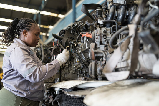 Automotive spare parts warehouse or auto parts warehouse. Female warehouse worker inspecting spare parts in auto parts warehouse. African American female worker checking old engine in garage