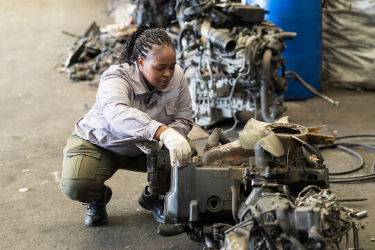 Automotive spare parts warehouse or auto parts warehouse. Female warehouse worker inspecting spare parts in auto parts warehouse. African American female worker checking old engine in garage - Powered by Adobe