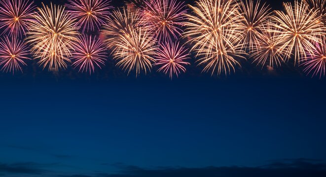 A stunning display of golden and pink fireworks bursting against a deep blue night sky, leaving ample copy space for celebratory text