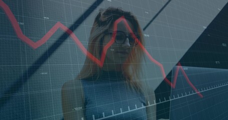 Analyzing data on red graph, woman standing in office lobby with gridlines, beams and glass panels