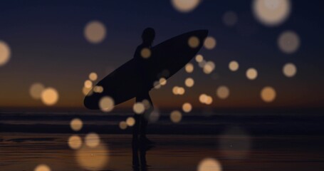 Walking wetsuit-clad surfer holding surfboard on wet sand at dusk, with bokeh orbs reflecting sky