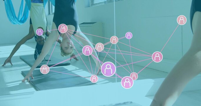 Female yoga practitioner bending forward on mat in studio, with aerial hammocks and network overlay - Powered by Adobe
