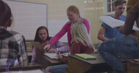 Collaborating teenage students pointing and discussing tablet around wooden desks in classroom