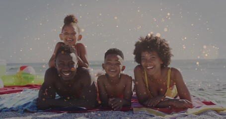Lying family in swimwear smiling on striped towels at shoreline, with swim ring and beach ball