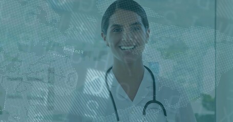 Smiling doctor standing at hospital glass panel, with stethoscope and digital map