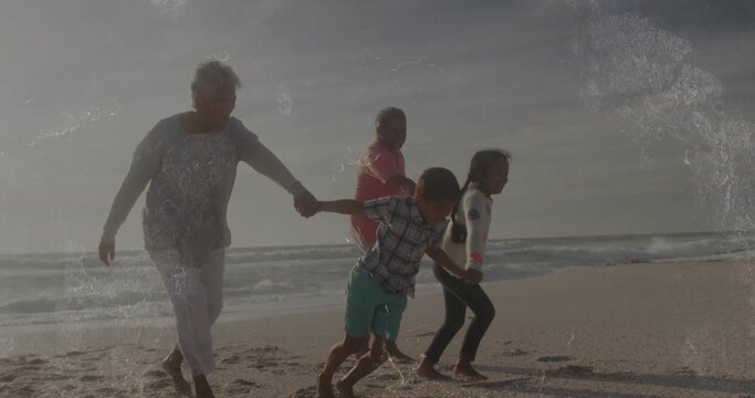 Running family of four holding hands on beach shore, with wet sand and ocean waves