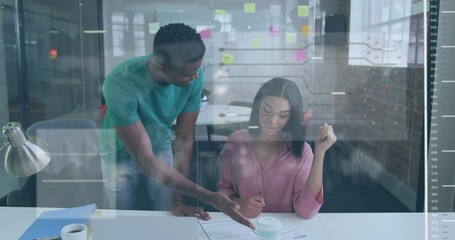 Pointing two colleagues collaborating over printed documents at office desk, showing sticky notes
