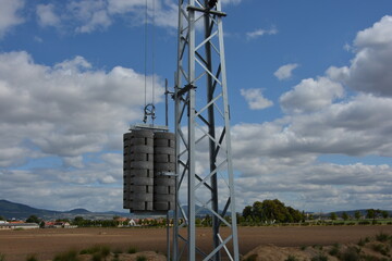 A galvanized steel lattice tower with heavy concrete counterweights, part of an electrical line in a rural landscape