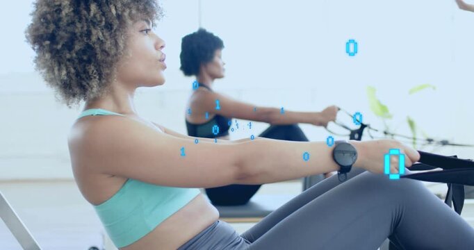 Two women on rowers initiating pull, generating binary code while fitness instructor guiding form