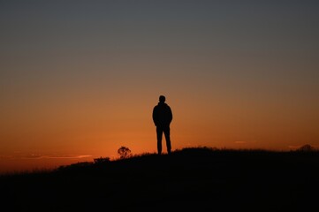 Fototapeta premium Silhouette of a man on a hill gazing at the majestic colors of the sunset in the sky
