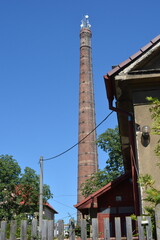 A very tall, old industrial brick chimney, now repurposed with communication antennas, stands against a clear blue sky