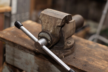 An old, weathered metal vise is securely mounted on a sturdy wooden workbench in a workshop setting.