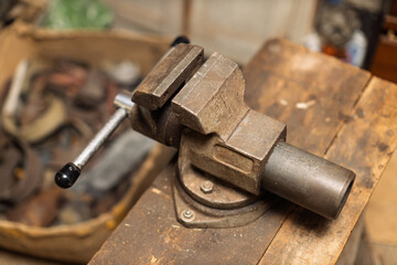 A sturdy, old metal bench vise sits on a wooden workbench in a cluttered workshop, ready for use.
