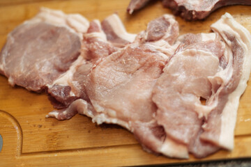 Several raw pork chops are neatly arranged on a light brown wooden cutting board, ready for meal...