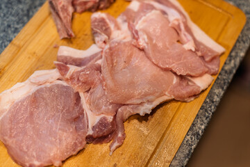 Various cuts of fresh, raw pork meat are arranged on a wooden cutting board, ready for cooking preparation.