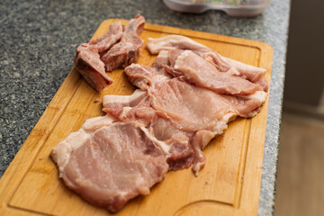 Various cuts of raw pork, including bone-in pieces and boneless slices, are arranged on a wooden cutting board, ready for preparation.