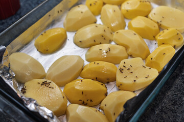 Peeled potatoes seasoned with caraway seeds are prepared in a foil-lined baking tray for cooking.
