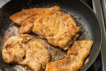Several golden-brown breaded cutlets are sizzling in oil within a black frying pan.
