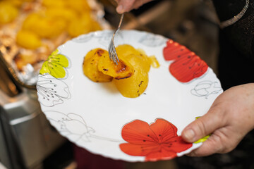 A person serves golden roasted potatoes, some with caramelized crust, onto a decorative white plate.