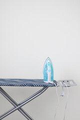 A modern iron standing on an ironing board against a plain white wall. Minimalist home interior concept with copy space. Clean, simple, and domestic lifestyle background. High quality photo