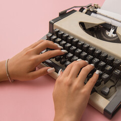 Hands typing on vintage typewriter, photographed from top angle on pink backdrop. Creative flat lay...