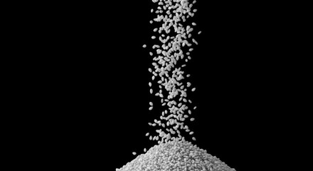 White rice grains falling down on a black background, creating a small pile
