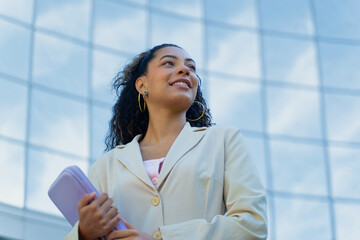 Smiling woman holding a folder, looking away with hope and vision in a modern city setting
