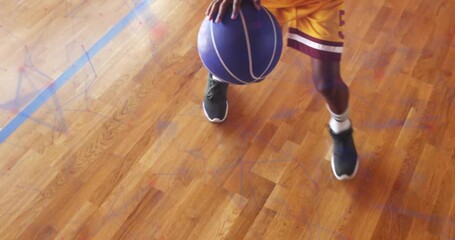Teenage boy crouching low in gym and pressing ball, performing dribbling drill for sports training - Powered by Adobe