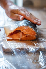 Fresh salmon being filleted by hand on wooden board with plastic wrap surface