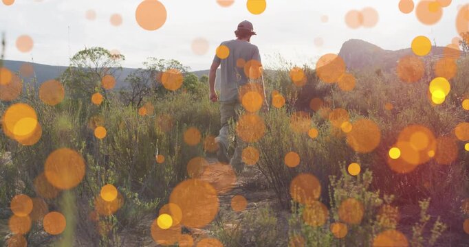 Male hiker exploring desert path while animated orange bokeh dots emerging and enhancing travel ads