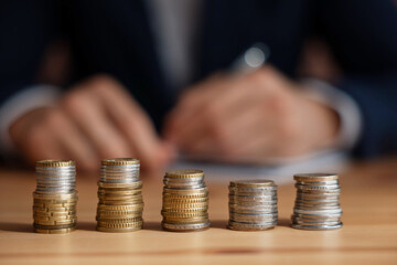 Man working at wooden table indoors, focus on stacks of coins
