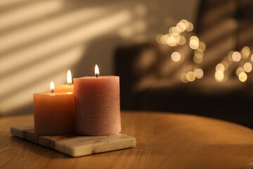 Burning candles on wooden table against blurred lights indoors, closeup. Space for text