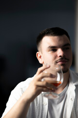 jeune homme avec un verre de cognac ou de whisky &agrave; la main en d&eacute;tente et d&eacute;gustation