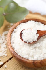 Sea salt in bowl, spoon and eucalyptus leaves on table, closeup
