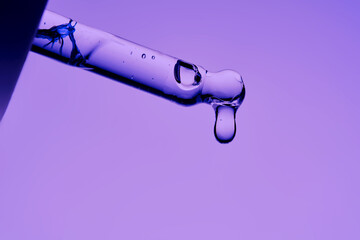 The texture of a cosmetic product with peptides in a pipette on a purple background.