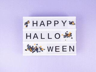 Happy halloween greetings on lightbox on purple background with black and orange confetti. Holiday kids party concept